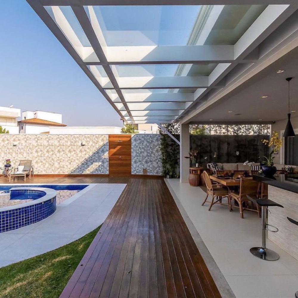 Área de lazer com cobertura de vidro sobre piscina e deck de madeira
